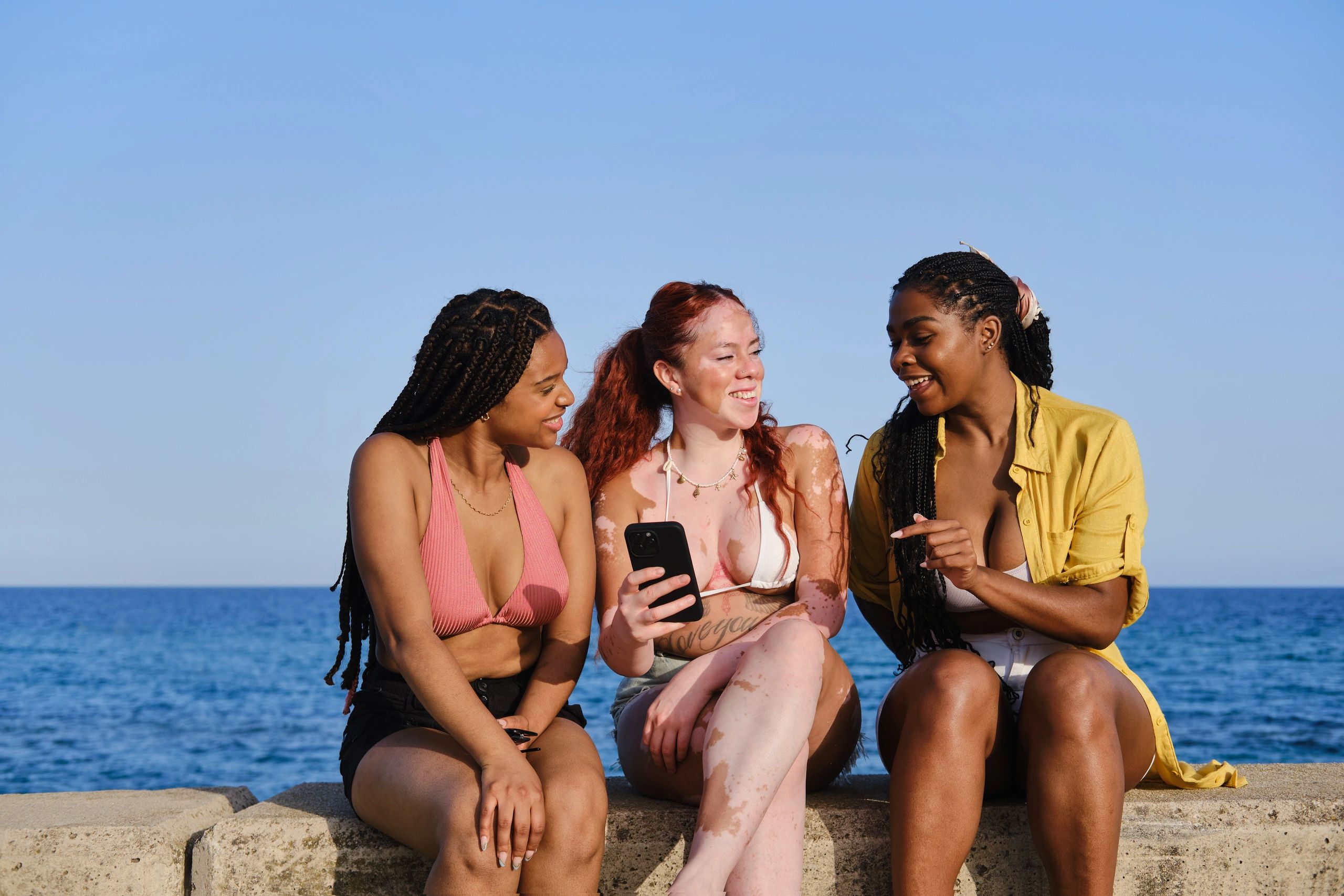 Friends checking a phone together by the sea